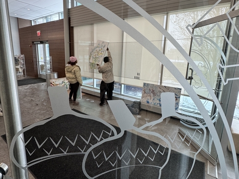 Two people hang a painting in the lobby of the Oak Park Michigan City Hall building.