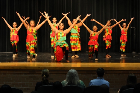 A group of costumed performers on stage with their arms upraised.