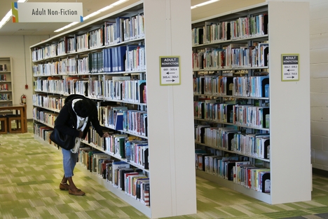 A women bends to pick a book from a shelf in the Oak Park Public Library.