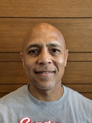 A the head shot of a bald man wearing a gray shirt smiling at the camera.