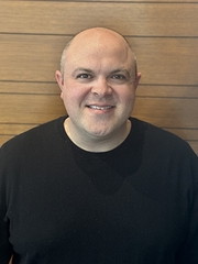 A head-and-shoulders photo of a bald man wearing a black shirt.