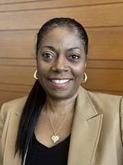 A head-and-shoulders photo of a woman with black hair wearing a tan jacket and black shirt.