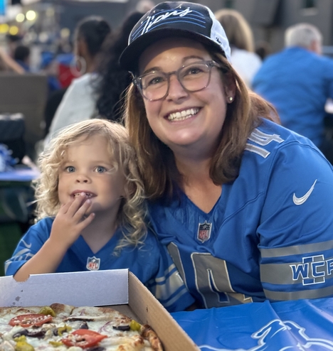 A women and young girl wearing Detroit Lions jerseys, smile at the camera.