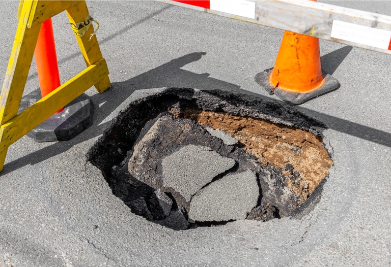 A barricade and cones surround a sinkhole in an asphalt road.