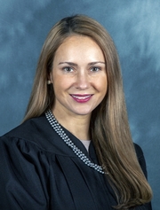 A woman with long brown hair wearing a judges robe smiles at the camera.