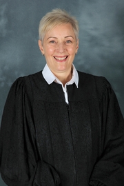 A woman with short blond hair wearing a judges robe smiles at the camera.
