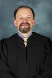 A man with short brown hair wearing a judges robe smiles at the camera.