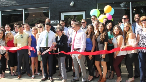 A women with large scissors cuts a ribbon in front of a business while a group stands around her.