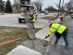 Two men repairing a sidewalk unload cement from a truck.
