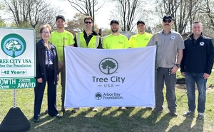 Several people hold a Tree City USA banner in a wooded area in Oak Park Michigan.