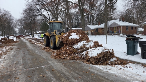 A tractor with a blade scoops leaves from a residential street in Oak park.