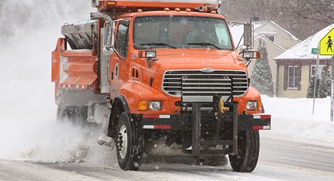 An orange snow plow scrapes snow from a residential street in Oak Park, Michigan.
