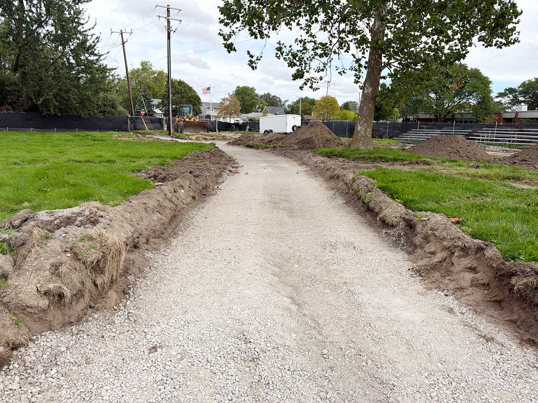 A dirt road in a grassy area with construction equipment in the background.