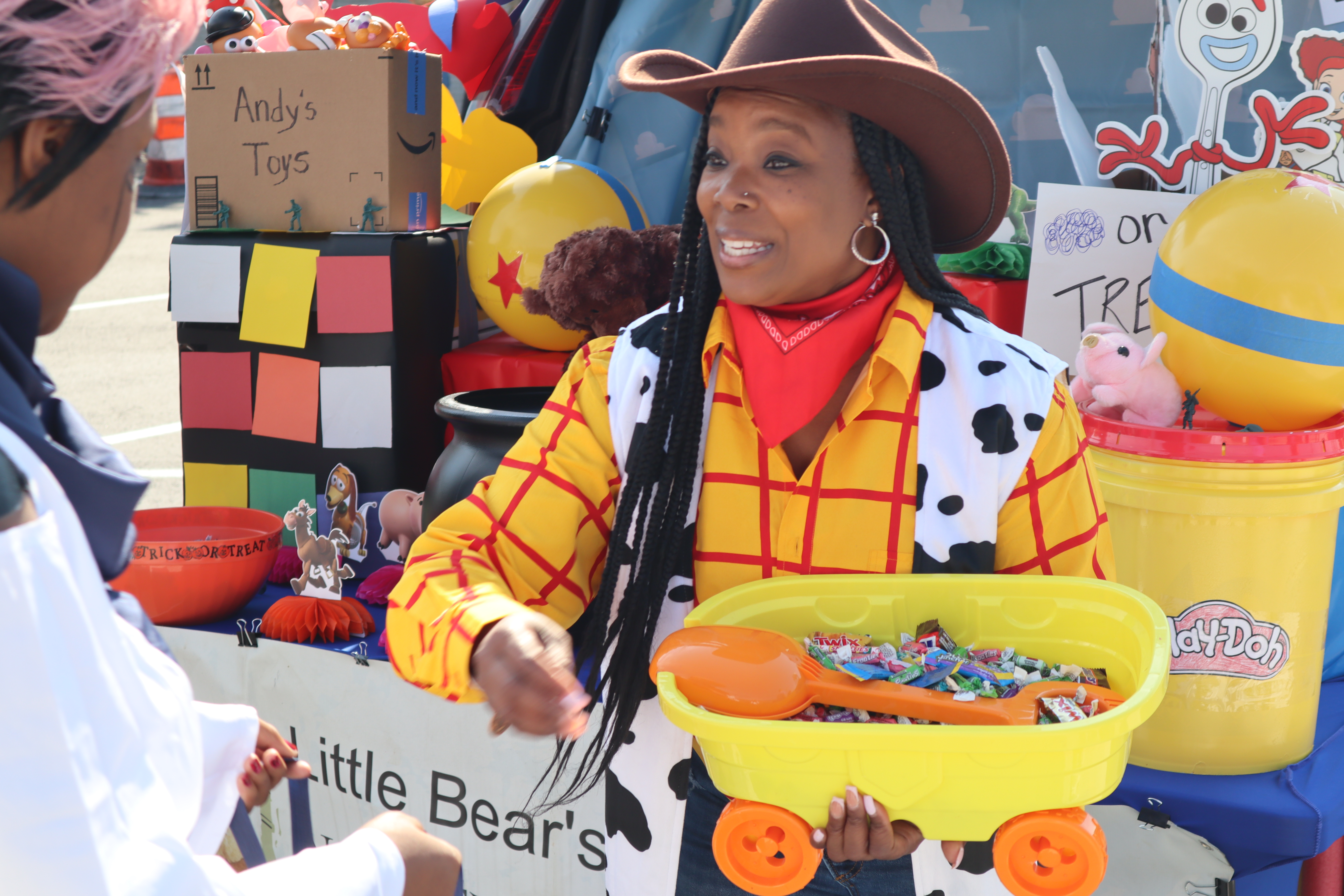 A women dressed as Andy from Toy Story hands out candy at a trunk or treat event.