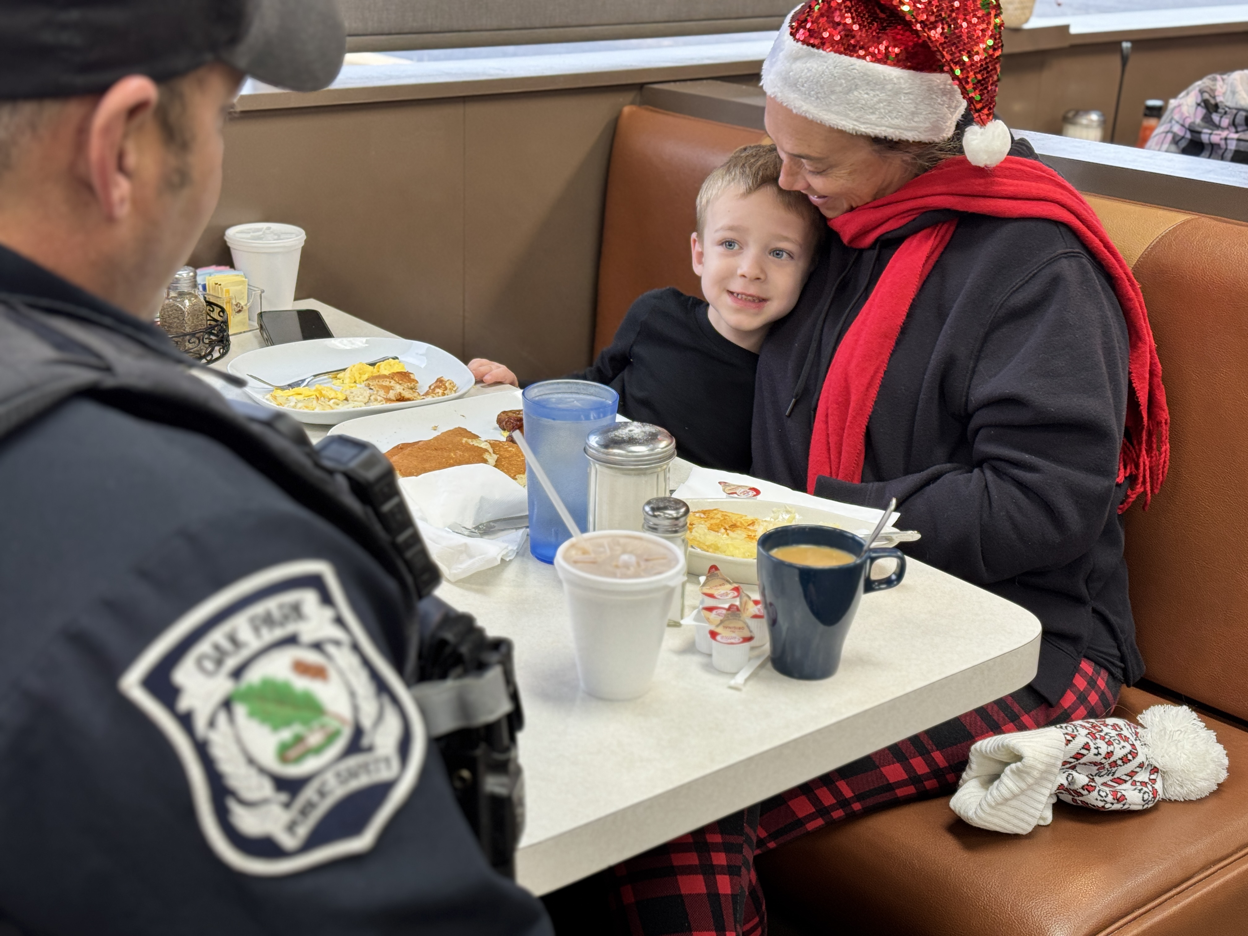 A uniformed police officer talks with a woman and young child in a restaurant.