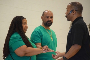A man in a black shirt gives instructions to a couple in matching green shirts. 