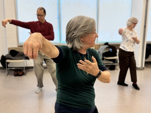 Three people practice tai chi moves in a large room.