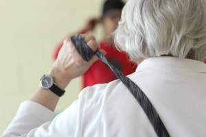 A woman with gray hair stretches a stap across her back in a chair yoga class.