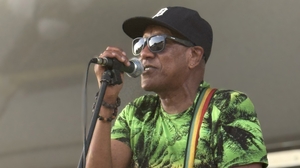 A man wearing a black hat and bright green shirt signs into a microphone.