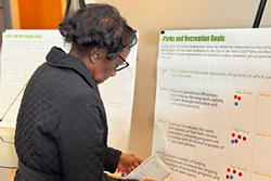 A senior woman in a black coat reads a large piece of paper displayed on an easel.