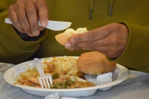 A person spreads butter on a piece of bread over a plate of food.