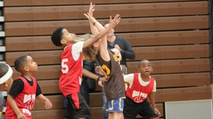 A group of boys in basketball uniforms reach up for a ball.