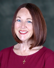 A headshot of a woman with short red hair and blue eyes wearing a red blouse.