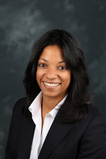 A headshot of a woman with black hair wearing a white blouse and black jacket smiling at the camera.