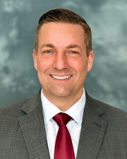 A head and shoulders shot of a man with short hair in a gray suit and white shirt.