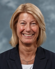 A headshot of a woman with blond hair wearing a white blouse and black jacket smiling at the camera.
