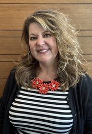 A head-and-shoulders photo of a woman with brown hair wearing a black and white blouse and black sweater.