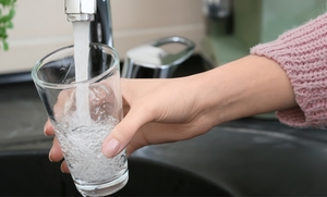 A person fills a glass with water at a kitchen sink.